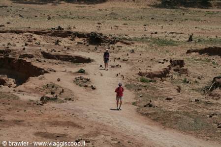 Two tourists walk along a sandy path in dry rocky terrain