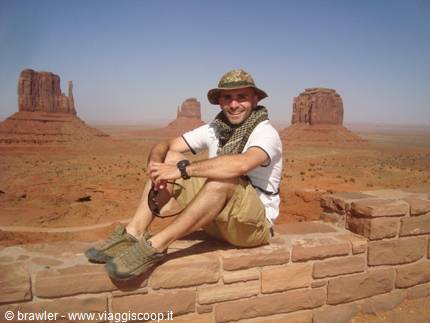 Smiling tourist sitting on a red stone wall, Monument Valley buttes behind