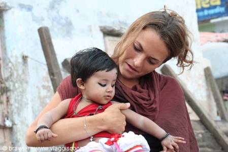 Blonde woman in a maroon scarf holding a toddler by a weathered wall