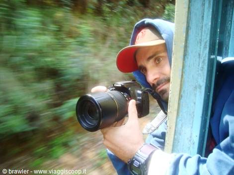 Hooded photographer with telephoto lens leaning out of a moving train window