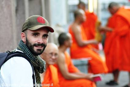 Traveler in green cap next to seated Buddhist monks in orange robes