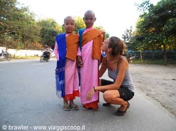 Woman crouching beside two young novice monks in pink and orange robes on the road