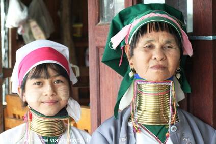 Padaung women wearing brass neck rings and green headscarf by wooden door