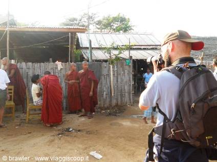 Photographer with backpack takes pictures of Buddhist monks in red robes near wooden houses