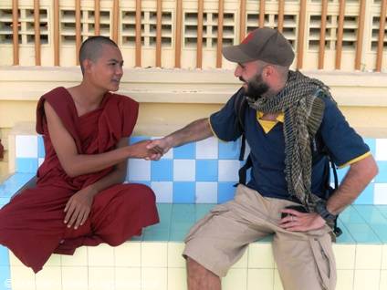 Traveler shakes hands with a Buddhist monk in maroon robes on tiled bench