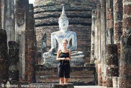 Tourist in front of a large seated stone Buddha among ancient columns, Sukhothai