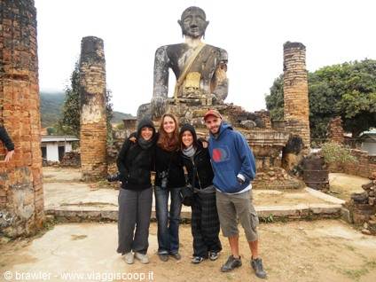 Four tourists pose before a large brick Buddha among temple ruins, grey light