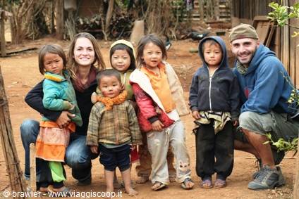 Two travelers crouching with five local children on dirt ground by wooden houses