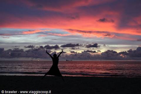 Woman's silhouette jumping with raised arms on the beach, fiery sky