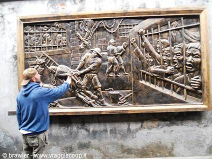 Tourist touches a bronze relief depicting prisoners behind bars