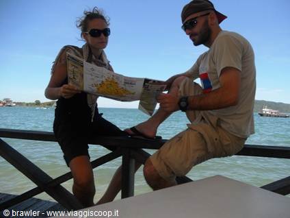 Two travelers read a map on a wooden jetty by the sea