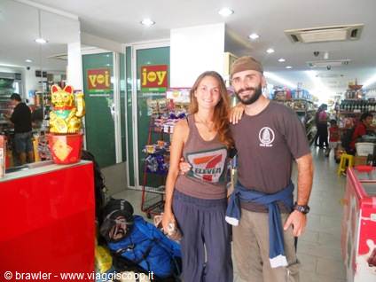 Smiling couple with backpacks inside a minimarket, next to a lucky cat