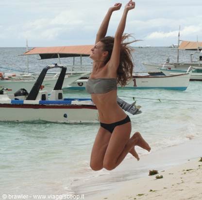 Woman jumping mid-air on the beach in front of traditional outrigger boats
