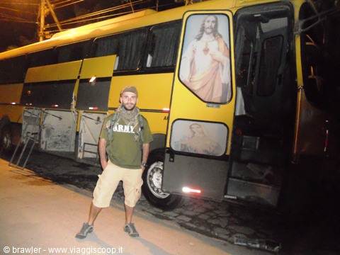 Traveler in green shirt beside a yellow bus decorated with a Jesus image