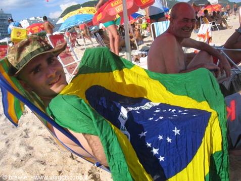 Tourist wrapped in Brazilian flag on beach chair, crowded umbrellas behind