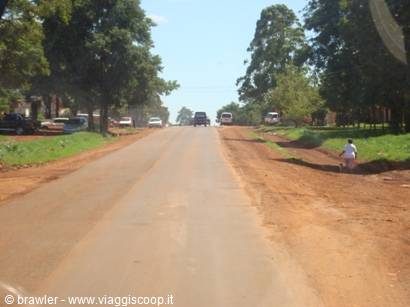 Red dirt road with cars in the distance and a child walking among greenery