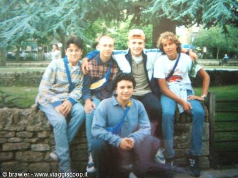 Five friends sitting on a stone wall in a park with conifer trees