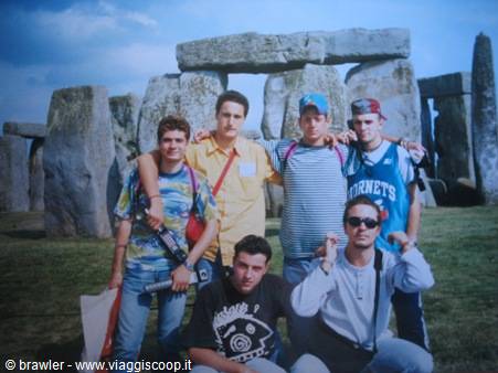 Five friends pose on the grass in front of Stonehenge's megaliths, cloudy sky