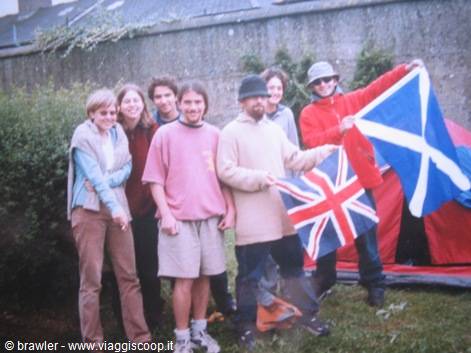 Group of friends at campsite holding Union Jack and Scottish flags by tents