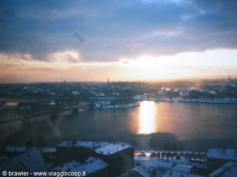 Frozen river among snowy rooftops, bridge and cloudy sky lit by the sun