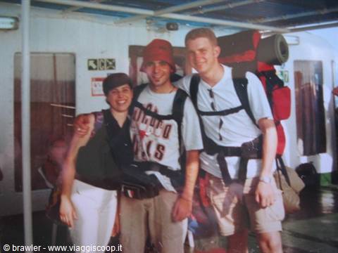 Three smiling backpackers with large backpacks on a ferry deck