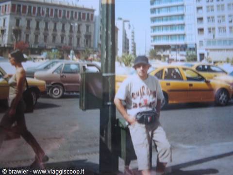 Tourist in hat sitting beside a kiosk, yellow taxis on the street