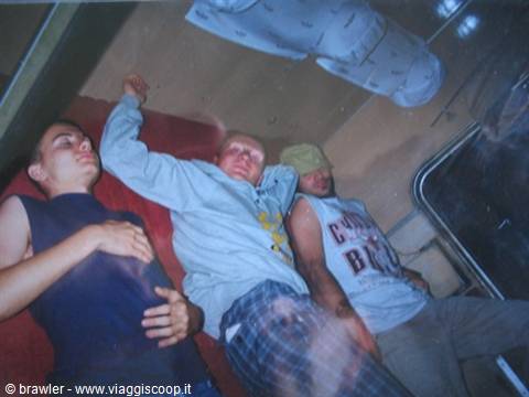 Three boys sleeping on a red bunk inside a dark bus
