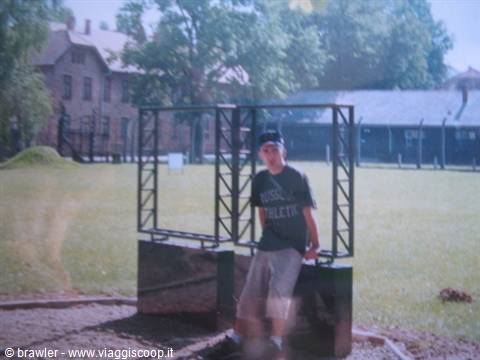 Boy sitting on a metal panel in a grassy yard with brick buildings
