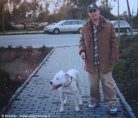 Young man in cap and brown coat walks white dog on paved path