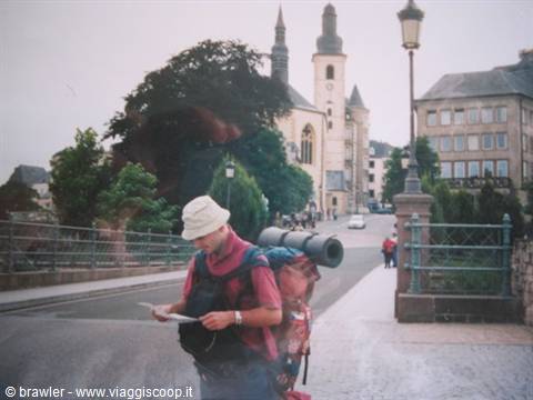 Backpacker with rolled mat checks his map on a bridge near a church