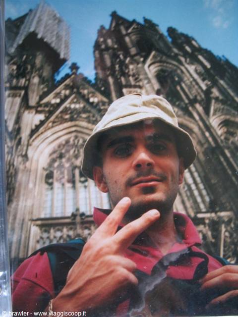 Young man in bucket hat making peace sign before Cologne Cathedral's gothic facade