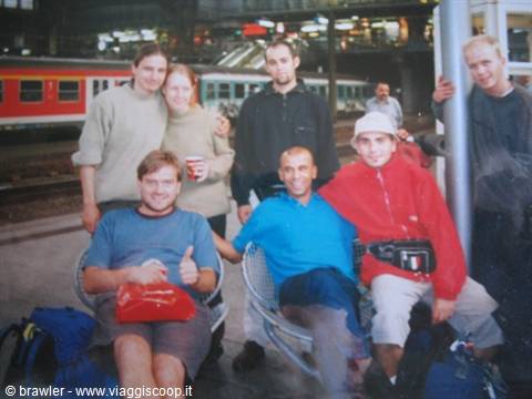 Group of friends posing on a railway station platform among backpacks and trains