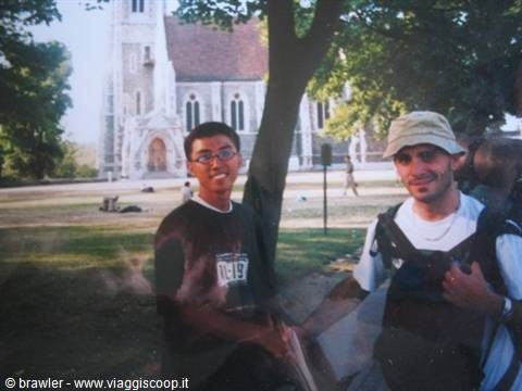 Two smiling backpackers under a tree in front of a white Gothic church