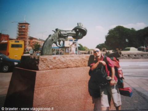 Backpacker posing next to the knotted gun sculpture in the city