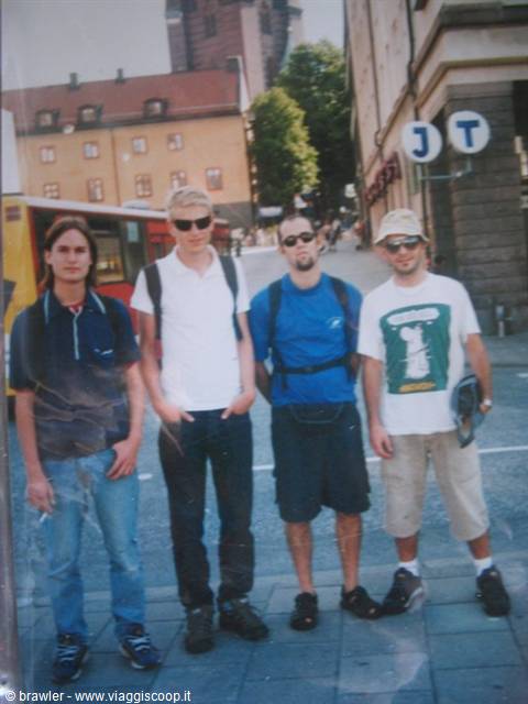 Four friends with backpacks pose on a sidewalk near Stockholm's T metro sign
