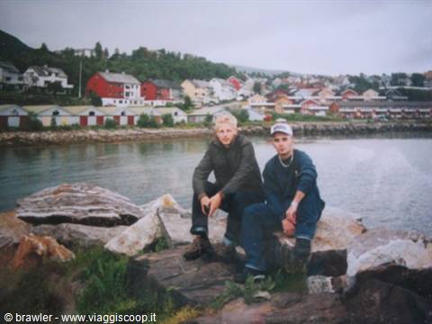 Two guys sitting on rocks in front of a fjord with colorful houses