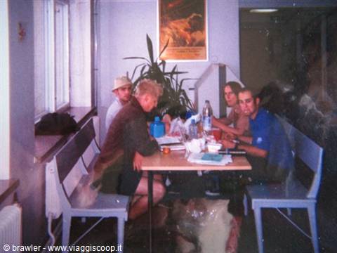 Four friends sitting at a table with bottles and food, hostel, daylight