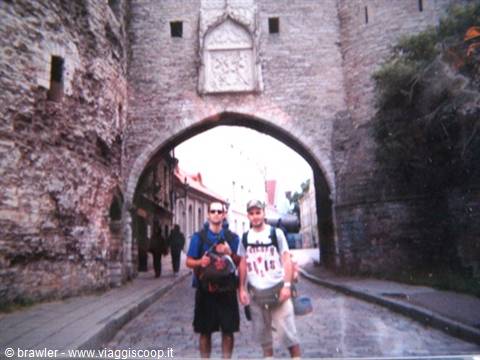 Two backpackers standing under the medieval stone gate of Tallinn