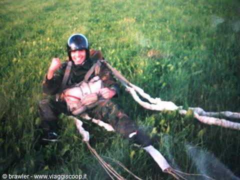 Paratrooper in helmet and harness grins sitting on grass after landing