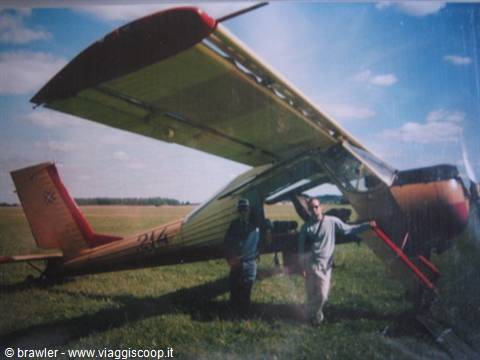 Two men beside a small yellow and red airplane on a grassy field