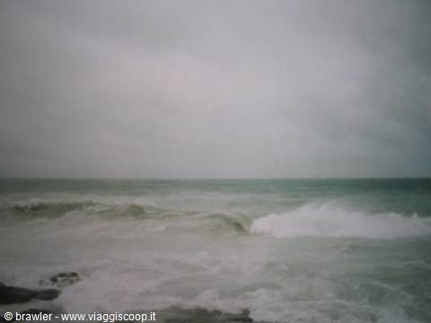 Foamy waves crash on wet rocks under a grey, cloudy sky