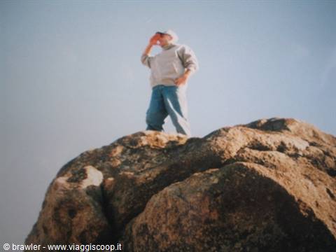 Boy in sweater and jeans standing on a large granite boulder, sunny light