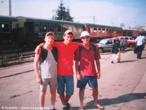 Three friends posing in front of train carriages at a station