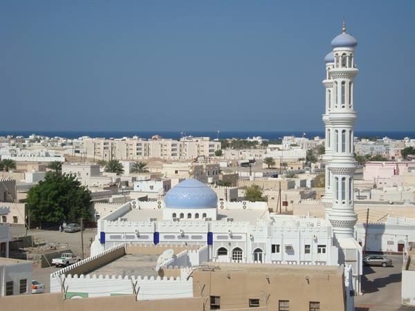 White mosque with blue dome and minaret, town and sea behind