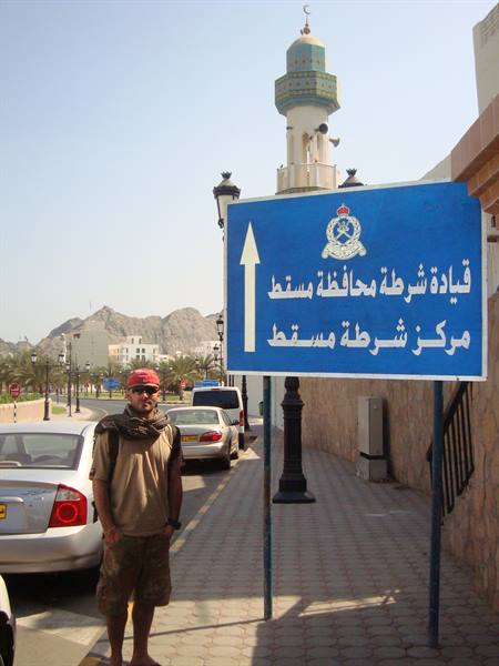 Traveler beside blue road sign, mosque minaret and mountains in background