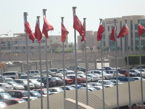 Red and white Bahraini flags waving above a crowded parking lot in Manama