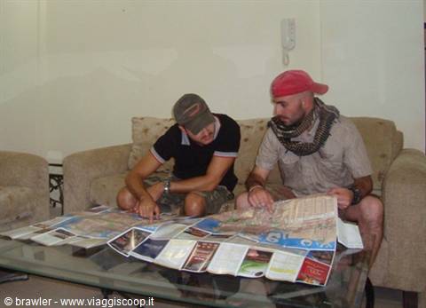 Two men in caps study maps and brochures on the glass coffee table