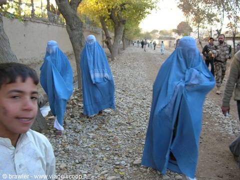 Women in blue burqas walking on a stony path, boy in foreground
