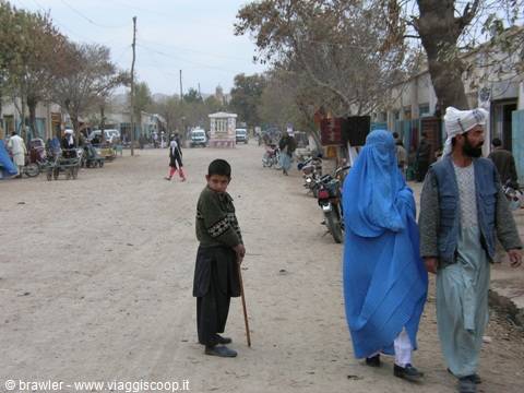 Boy with stick and woman in blue burqa walking on dusty street