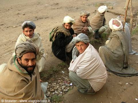 Men wearing turbans and shawls sitting on the ground on sandy terrain